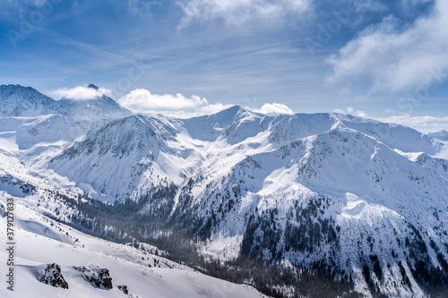 View from Kasprowy Wierch at pine forest with winter coating in the valley. Snow capped mountain peaks of Tatra Mountains, Bukowina Tatrzanska, Poland