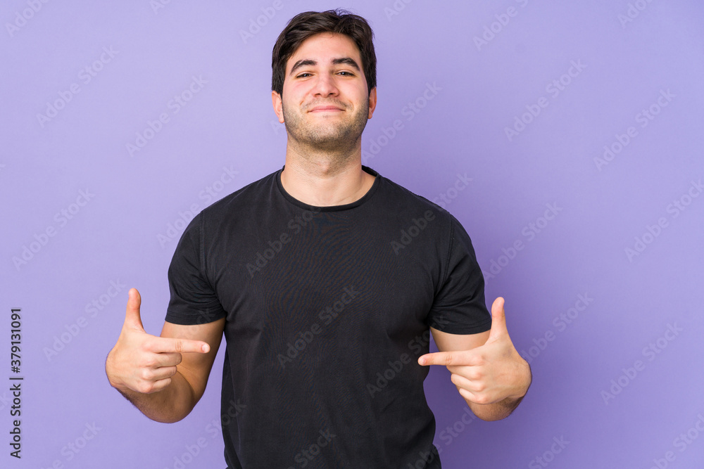 Fototapeta premium Young man isolated on purple background person pointing by hand to a shirt copy space, proud and confident