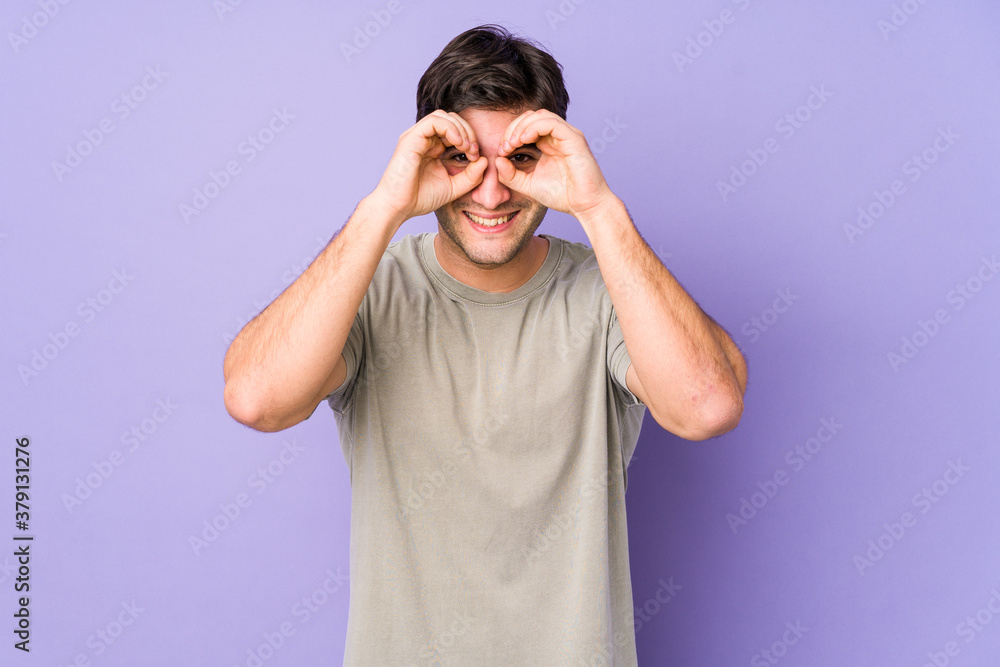 Young man isolated on purple background showing okay sign over eyes Young man isolated on purple background showing okay sign over eyes
