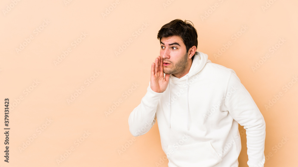 Young man isolated on beige background is saying a secret hot braking news and looking aside Young man isolated on beige background is saying a secret hot braking news and looking aside