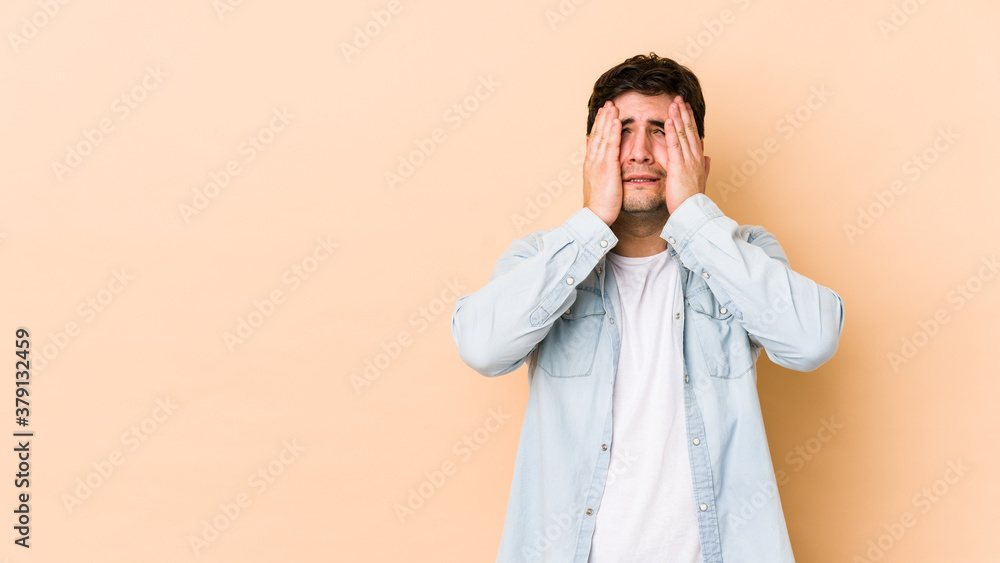 Young man isolated on beige background whining and crying disconsolately. Young man isolated on beige background whining and crying disconsolately.