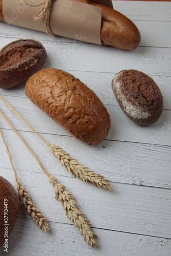 fresh bread - buns, baguette and ears of wheat on wooden background flat lay. Vertival image photo