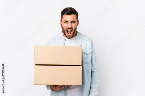 Young caucasian man moving to a new home isolated screaming very angry and aggressive.