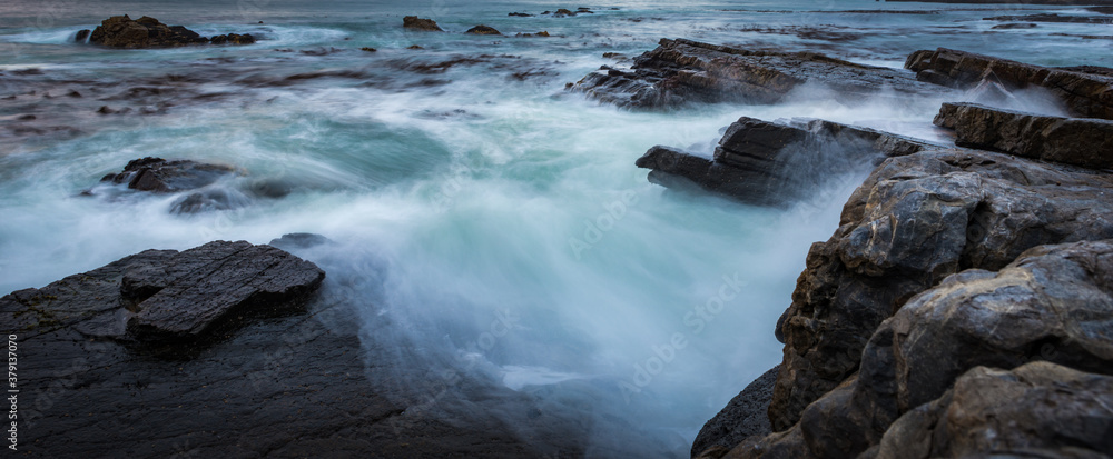 Fototapeta premium the power our oceans, closeup photography of the waves hitting into the rocks, and the water splashing up into the air during the sunset with beautiful cloudscape in the background 