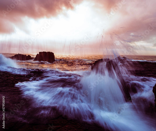 the power our oceans, closeup photography of the waves hitting into the rocks, and the water splashing up into the air during the sunset with beautiful cloudscape in the background 