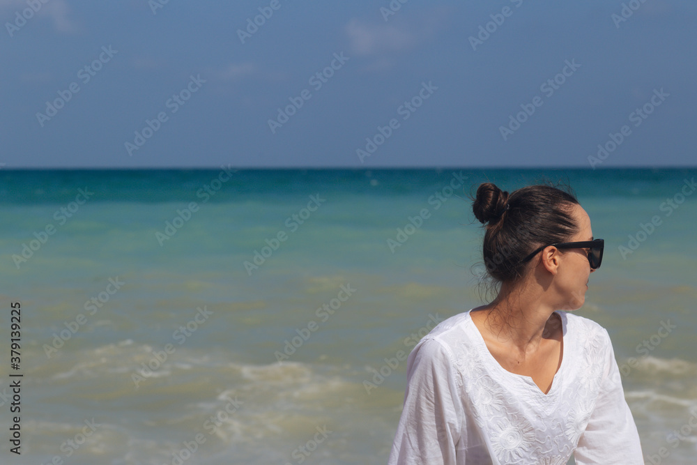 Young girl sitting on the beach after sunset in the sea background.Young traveler.Side view of serene woman sitting on beach against blue sky outdoors