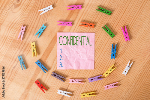 Conceptual hand writing showing Confidential. Concept meaning containing an individualal information whose unauthorized disclosure Colored crumpled papers wooden floor background clothespin photo