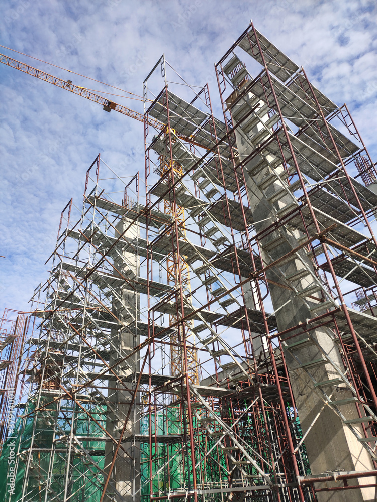 SELANGOR, MALAYSIA -AUGUST 4, 2020: Temporary stairs and scaffolding are used in the construction of high concrete columns. Scaffolding is wrapped with safety netting for safety purposes.