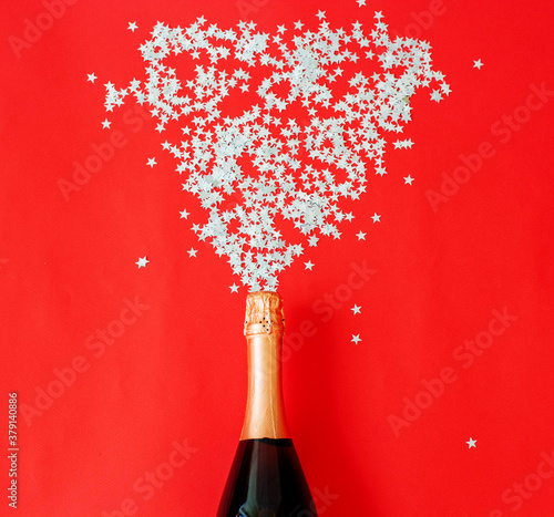 A flat layer of celebration. A bottle of champagne with colorful party streamers on a red background. The concept of new year and Christmas.