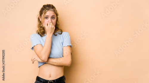 Young caucasian woman isolated on beige background biting fingernails, nervous and very anxious.