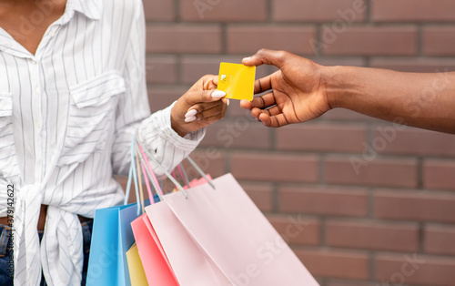 Female shopper with colored bags gives credit card to seller