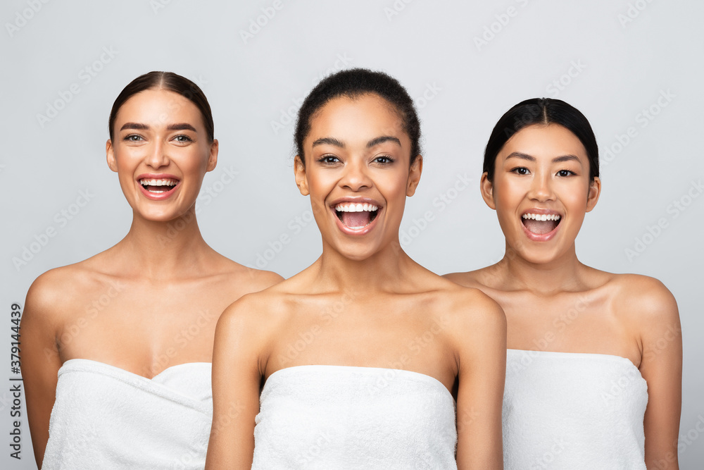 Playful Ladies Posing Wrapped In White Bath Towels, Gray Background Playful Ladies Posing Wrapped In White Bath Towels, Gray Background