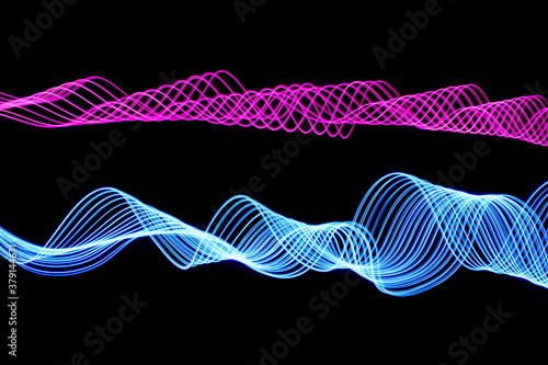 Long exposure photograph of neon pink and blue colour in an abstract swirl, parallel lines pattern against a black background. Light painting photography. photo