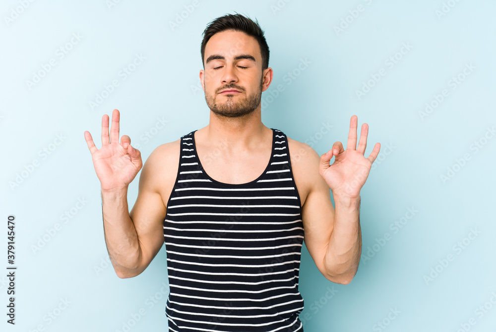Fototapeta premium Young caucasian man isolated on blue background relaxes after hard working day, she is performing yoga.