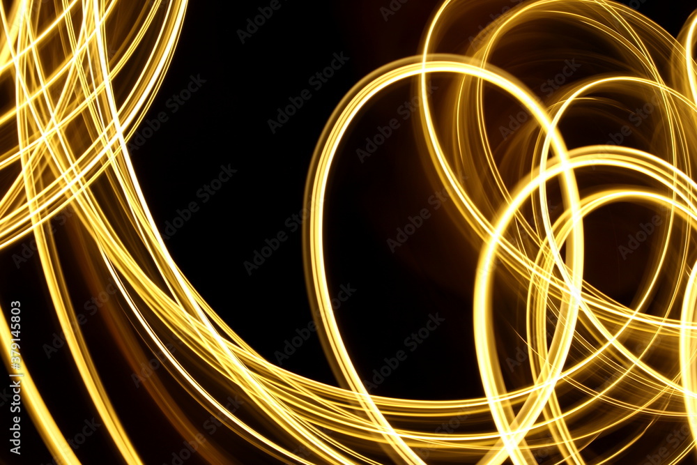 Long exposure photograph of neon gold colour in an abstract swirl, parallel lines pattern against a black background. Light painting photography. Long exposure photograph of neon gold colour in an abstract swirl, parallel lines pattern against a black background. Light painting photography.