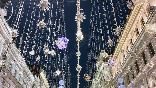 The street is decorated with luminous garlands of lights that sway in the wind against the background of the dark sky and buildings. Moscow. Nikitskaya street. photo