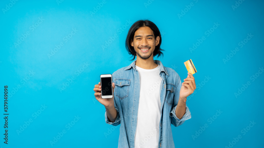 Asian Thai man with long hear and mustache holding phone with copy space on screen and show credit card on blue background in studio. Asian Thai man with long hear and mustache holding phone with copy space on screen and show credit card on blue background in studio.