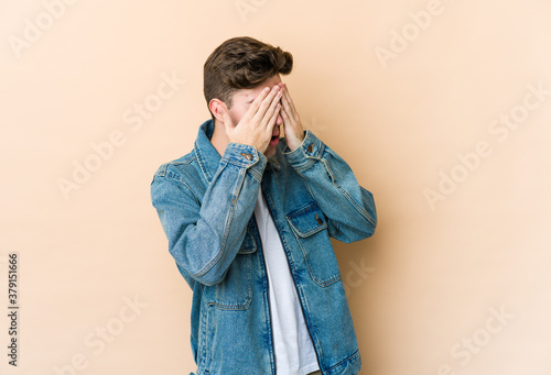 Young caucasian man isolated on beige background afraid covering eyes with hands.