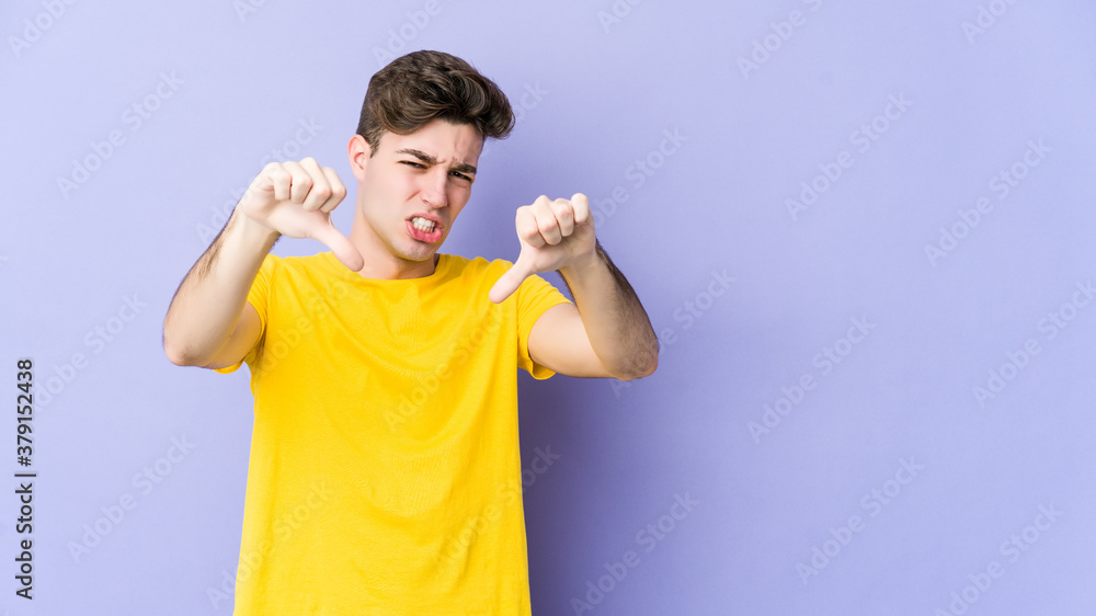 Young caucasian man isolated on purple background showing thumb down and expressing dislike. Young caucasian man isolated on purple background showing thumb down and expressing dislike.