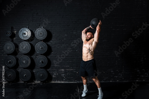 Young sweaty strong muscular fit man with big muscles doing ball throwing on the floor as hardcore cross workout training in the gym photo