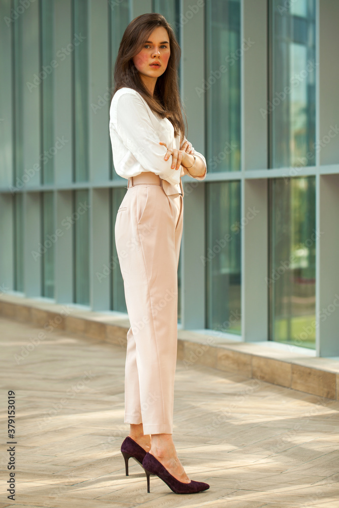 Young beautiful brunette woman in white blouse and pink pants in office Young beautiful brunette woman in white blouse and pink pants in office