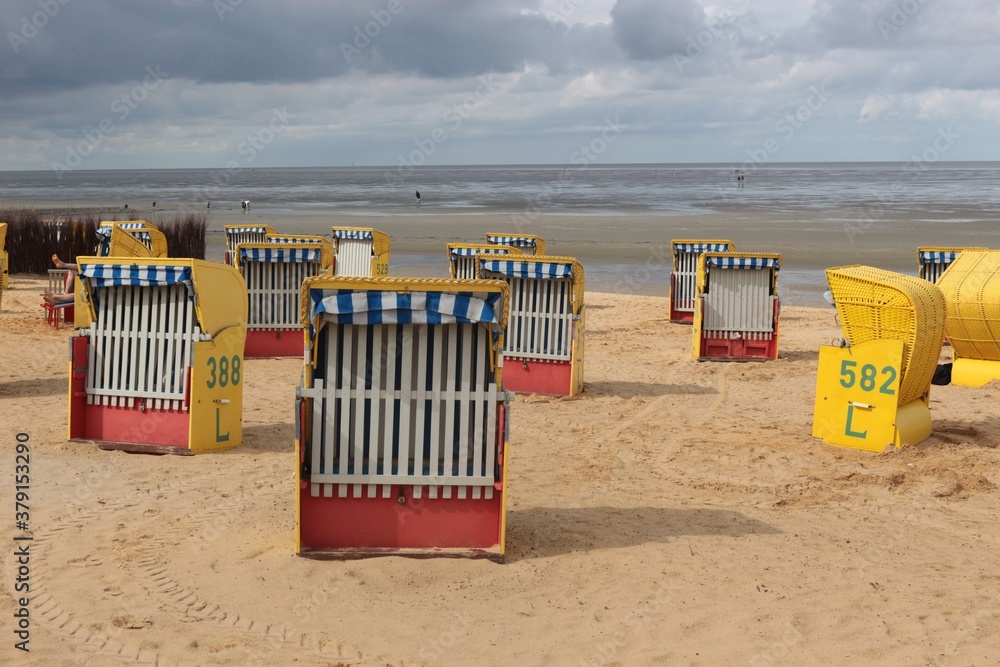 Beach chairs on a sandy beach by the North Sea. View of the wadden sea. Cuxhaven, North Germany, Europe.