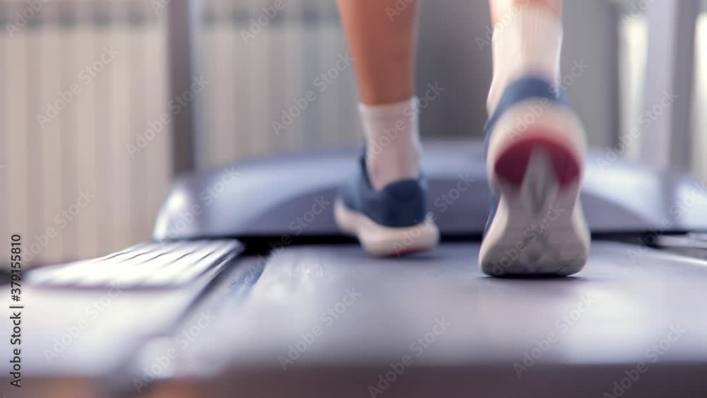 Closeup athletic feet running on treadmill in fitness gym. Back view. Low view sneakers training in sport club. Concept of sports training, weight loss, self-improvement Closeup athletic feet running on treadmill in fitness gym. Back view. Low view sneakers training in sport club. Concept of sports training, weight loss, self-improvement