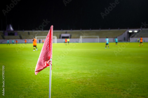 Close-up at football pitch corner flag with blurred of unrecognized football playing/action match. Sport and recreation concept background.