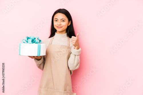Young chinese woman holding a cake isolated smiling and pointing aside, showing something at blank space.
