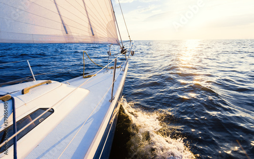 White sloop rigged yacht sailing in an open Baltic sea at sunset. Dramatic sky with glowing clouds, golden sunlight. Travel destinations, cruise, sport, recreation, leisure activity, transportation photo