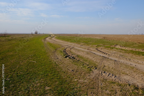A narrow dirt road in an evening field. Clear blue sky over the field.