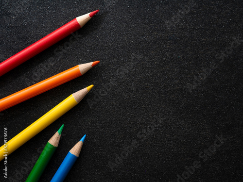 Bright colored pencils on a dark black background. Seven colors of the rainbow. Back to school. Education and creativity. Drawing and art. Free space for text.