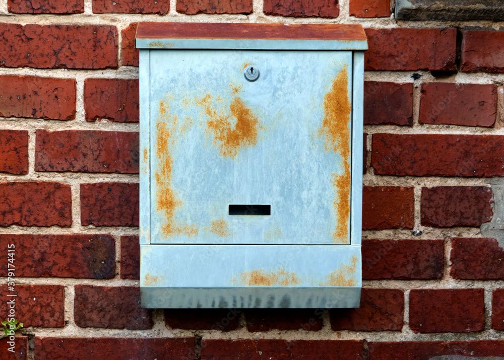 Uninscribed grey mailbox with rust stains on a red spotted brick wall, concept
