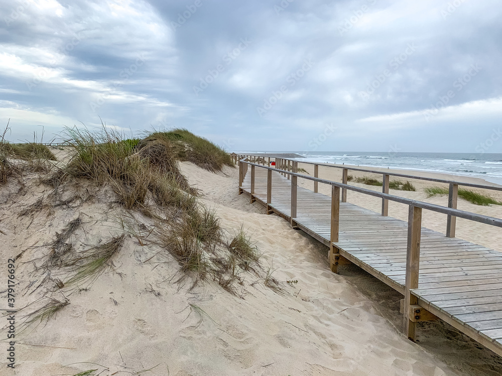 Obraz premium Boardwalk near the sand dunes in Costa Nova, Portugal with the ocean in the background