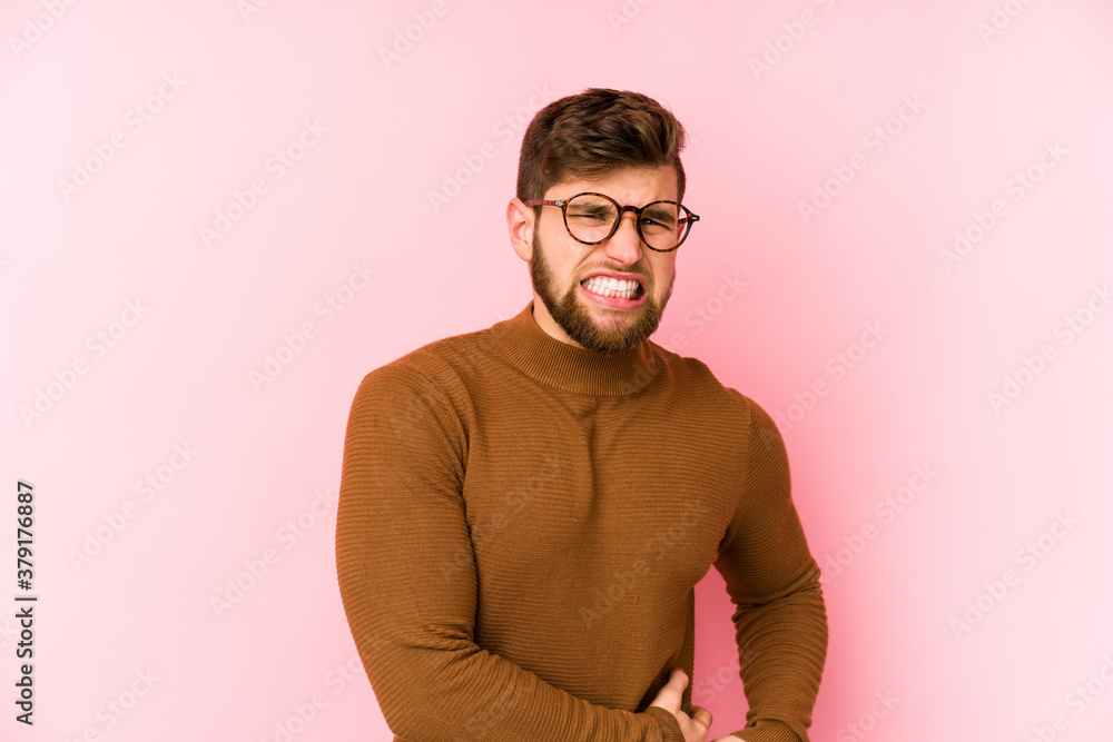 Young caucasian man isolated on pink background having a liver pain, stomach ache.