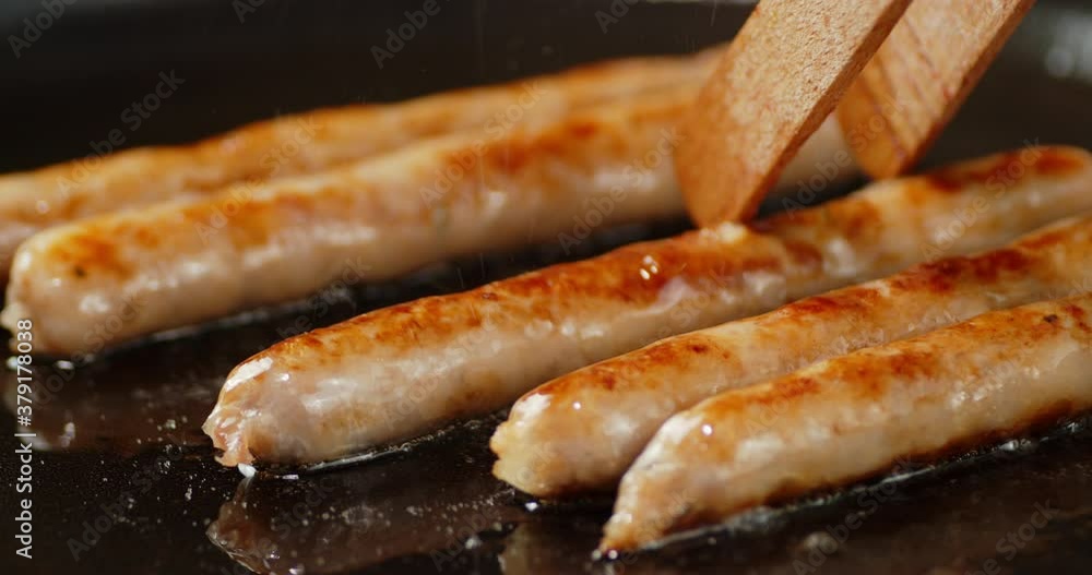 Fried sausage is turned over on pan with a wooden spatula. Fried sausage is turned over on pan with a wooden spatula.