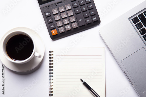 Top view of working space with blank notebook page, laptop,calculator, hot coffee and pen. Top view. Business planning concept on white.