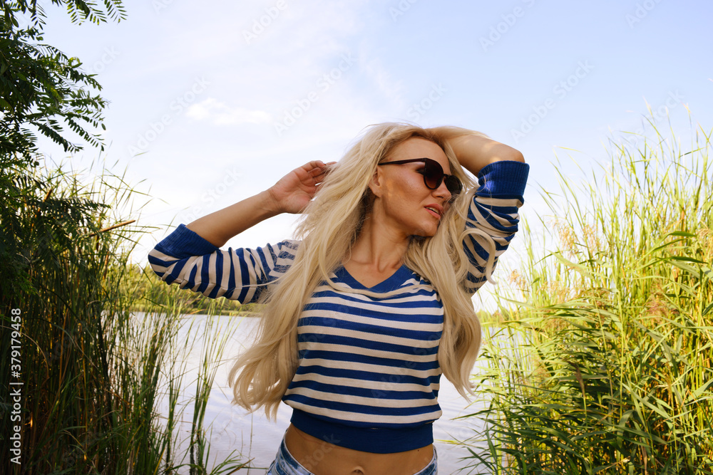 Portrait of a young blonde woman in sunglasses and a sweater on nature near the lake