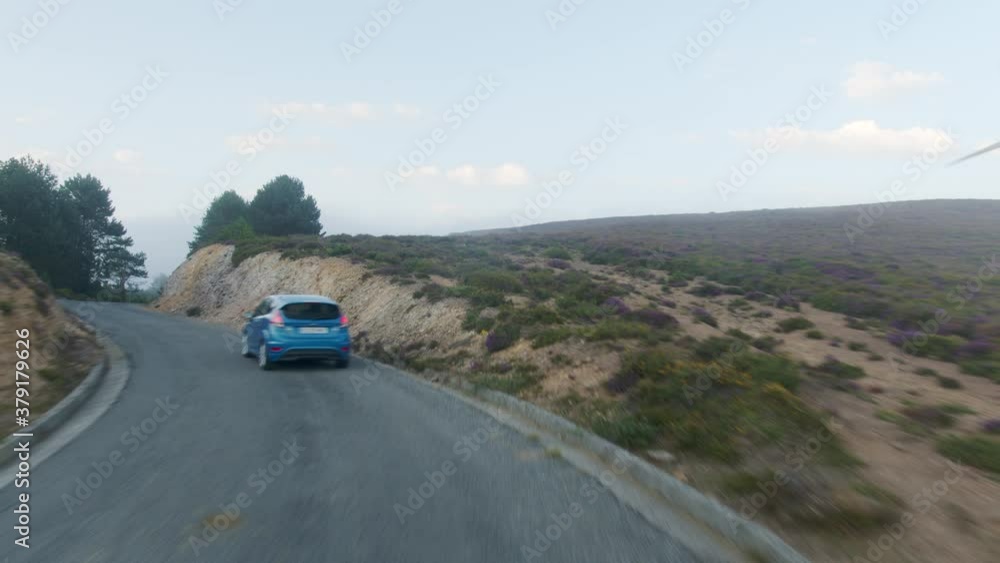 Car drives along a mountain road, while camera follows it from above, wind turbines on the background Car drives along a mountain road, while camera follows it from above, wind turbines on the background