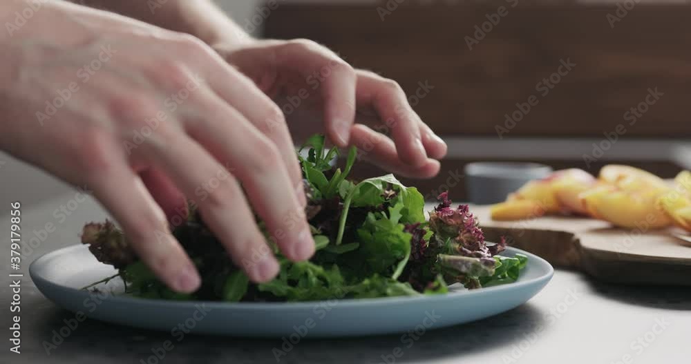Slow motion man making salad with nectarines and mozzarella on a blue plate on concrete countertop on kitchen, add greens