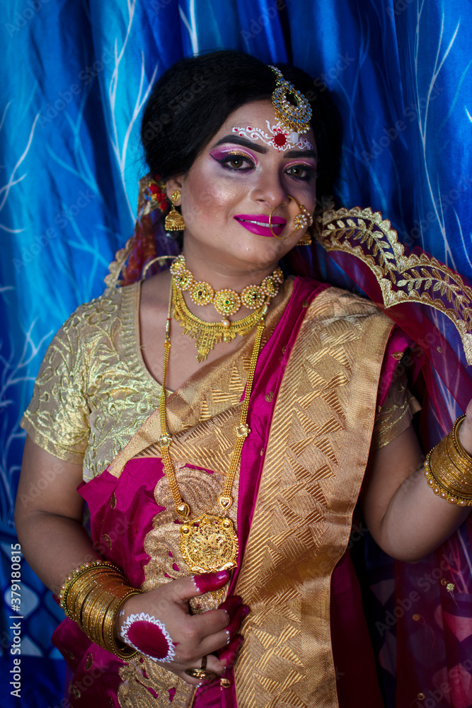 Portrait of a cute Indian model in Bridal look with heavy gold jewelry and red sari