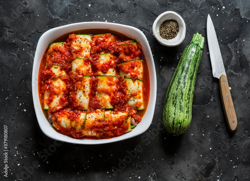 фотографія Preparing zucchini cannelloni with tomato sauce in a baking dish on a dark background, top view
