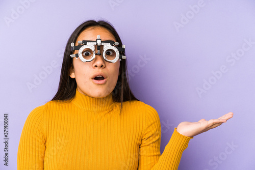 Youn indian woman with optometry glasses impressed holding copy space on palm.