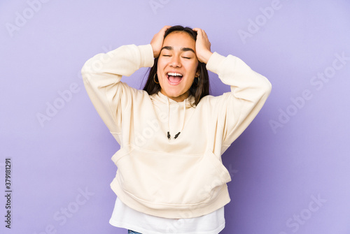 Young woman isolated on a purple background laughs joyfully keeping hands on head. Happiness concept.