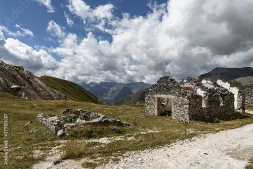 In the foreground a mountain pass in the alps ruins of a mitilitaries customs house between France and Italy. In the background the mountains, the clouds and the blue sky,
