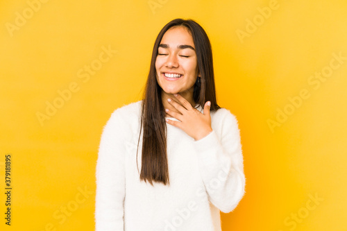 Young woman isolated on a yellow background laughs out loudly keeping hand on chest. © Asier