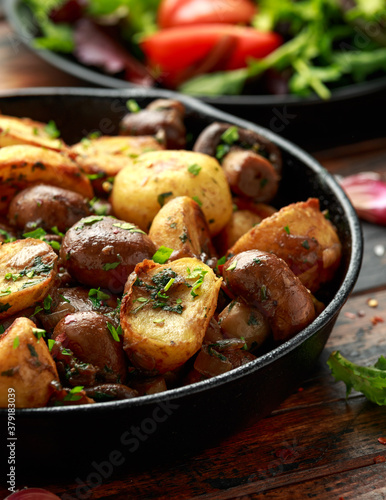 Baked potato with mushrooms and herbs in iron cast pan on wooden table