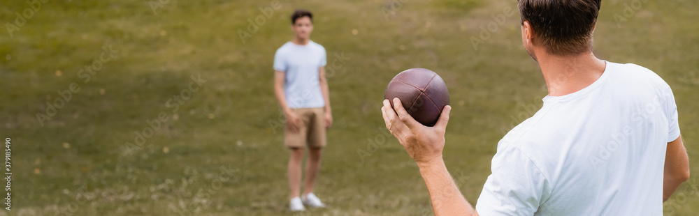 Fototapeta premium panoramic concept of father holding rugby ball near teenager son in green park