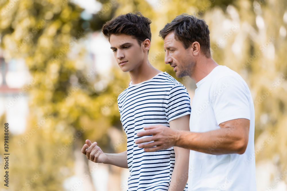 father gesturing and talking with teenager son in park - obrazy, fototapety, plakaty 