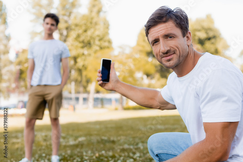 selective focus of father holding smartphone with blank screen near teenager son in park